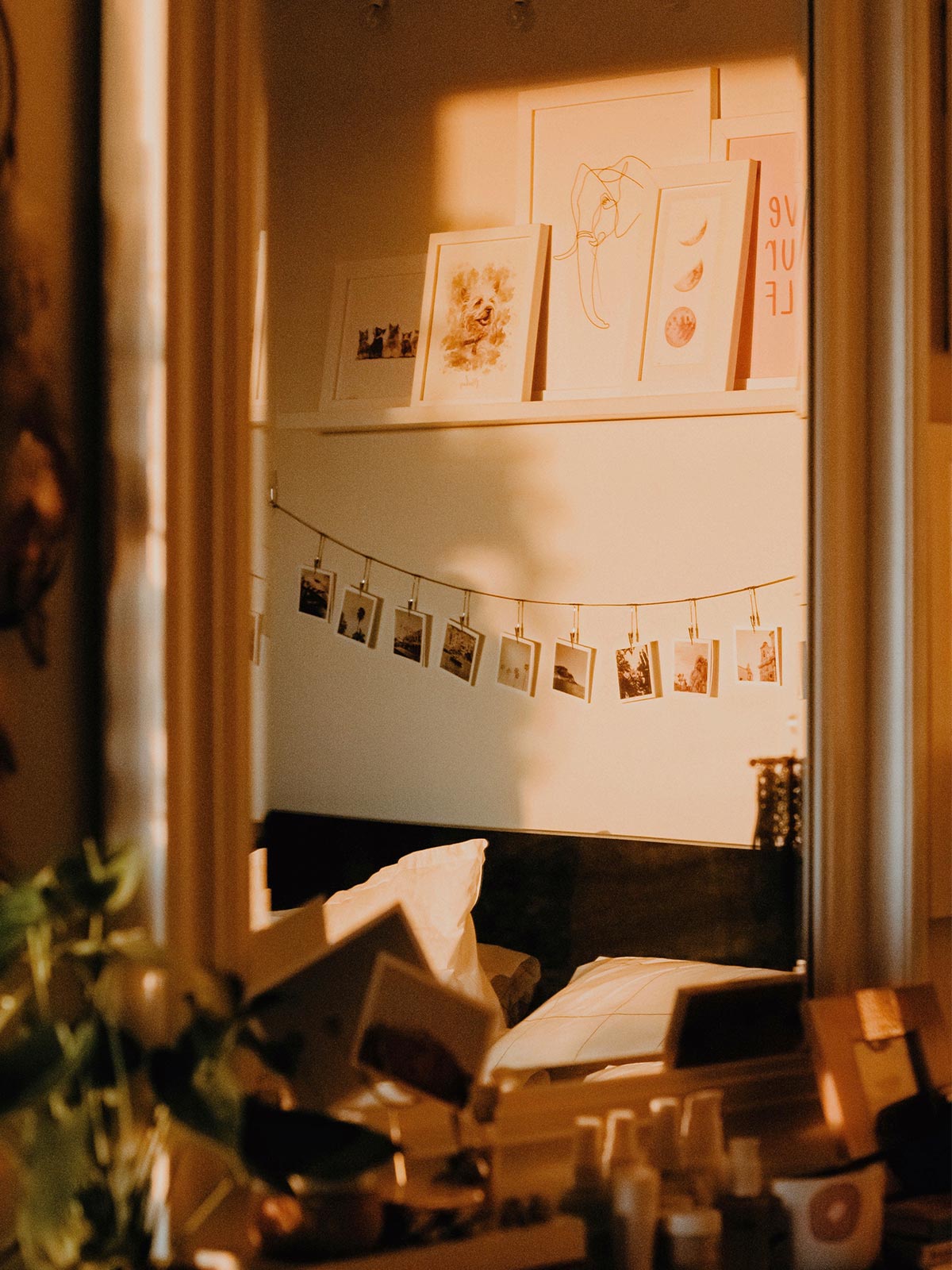 Artifact Uprising square photo prints hanging from string above bed and below a floating shelf filled with framed prints