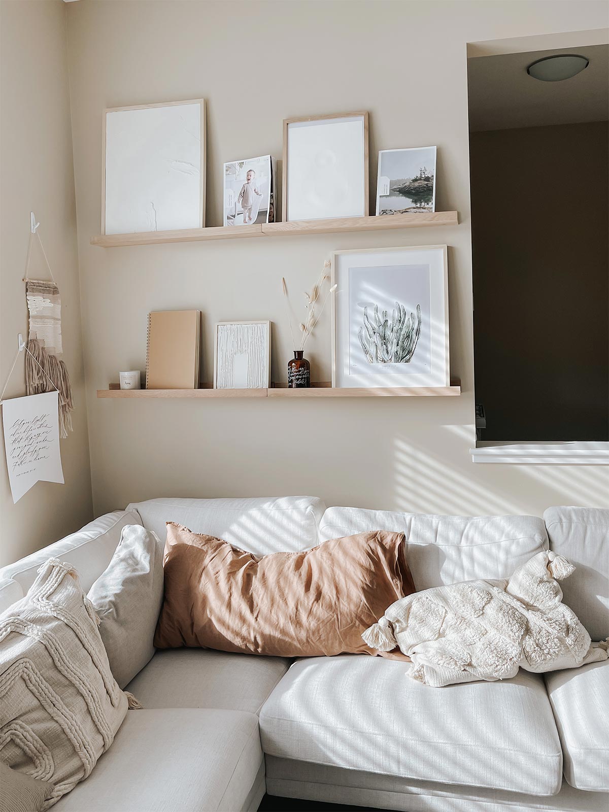 Photo frames and other decorative items on floating wood ledges above cream sectional couch