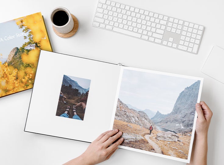 Photo book and cup of coffee on desk next to keyboard