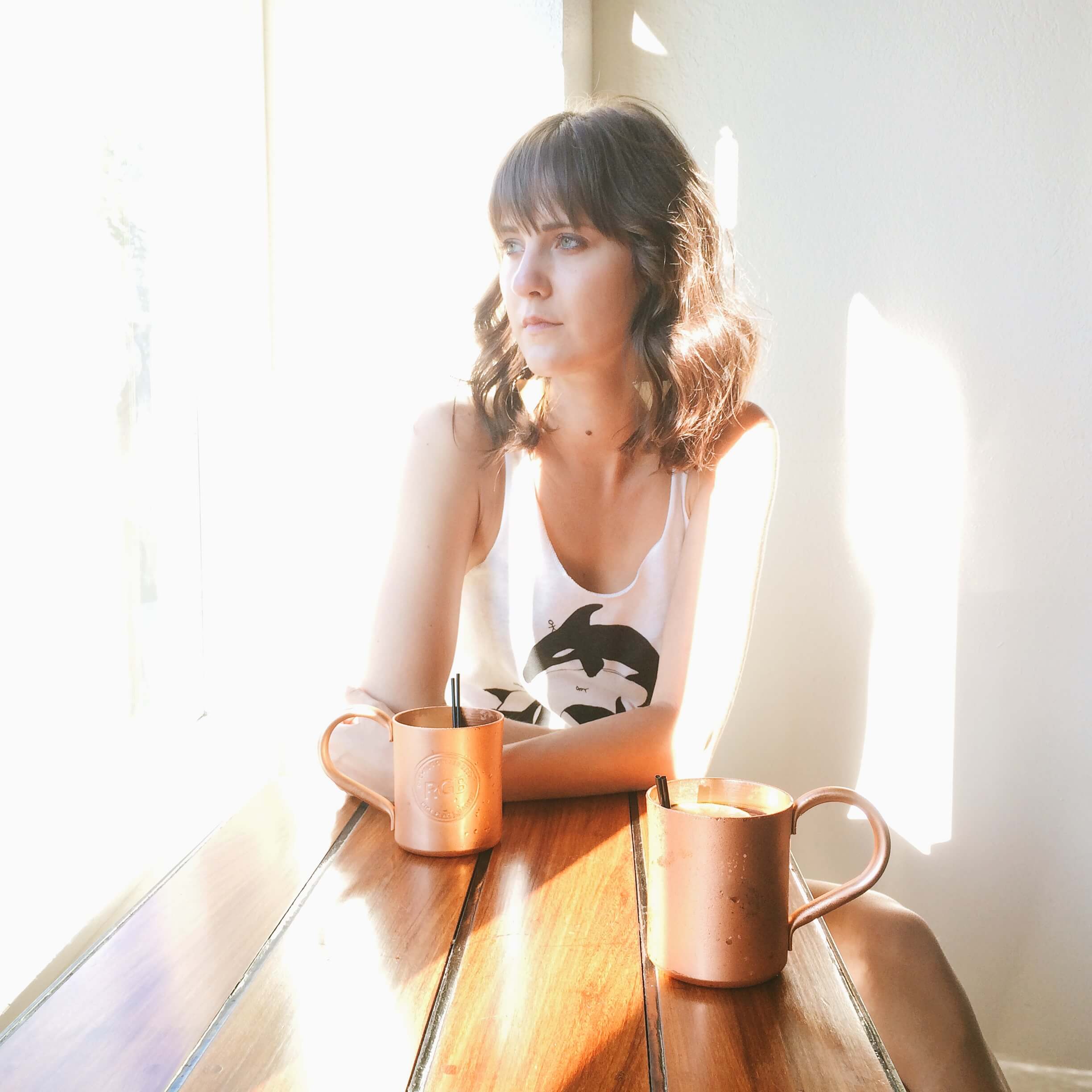 Photo of woman shrouded in light drinking Moscow Mule next to a window