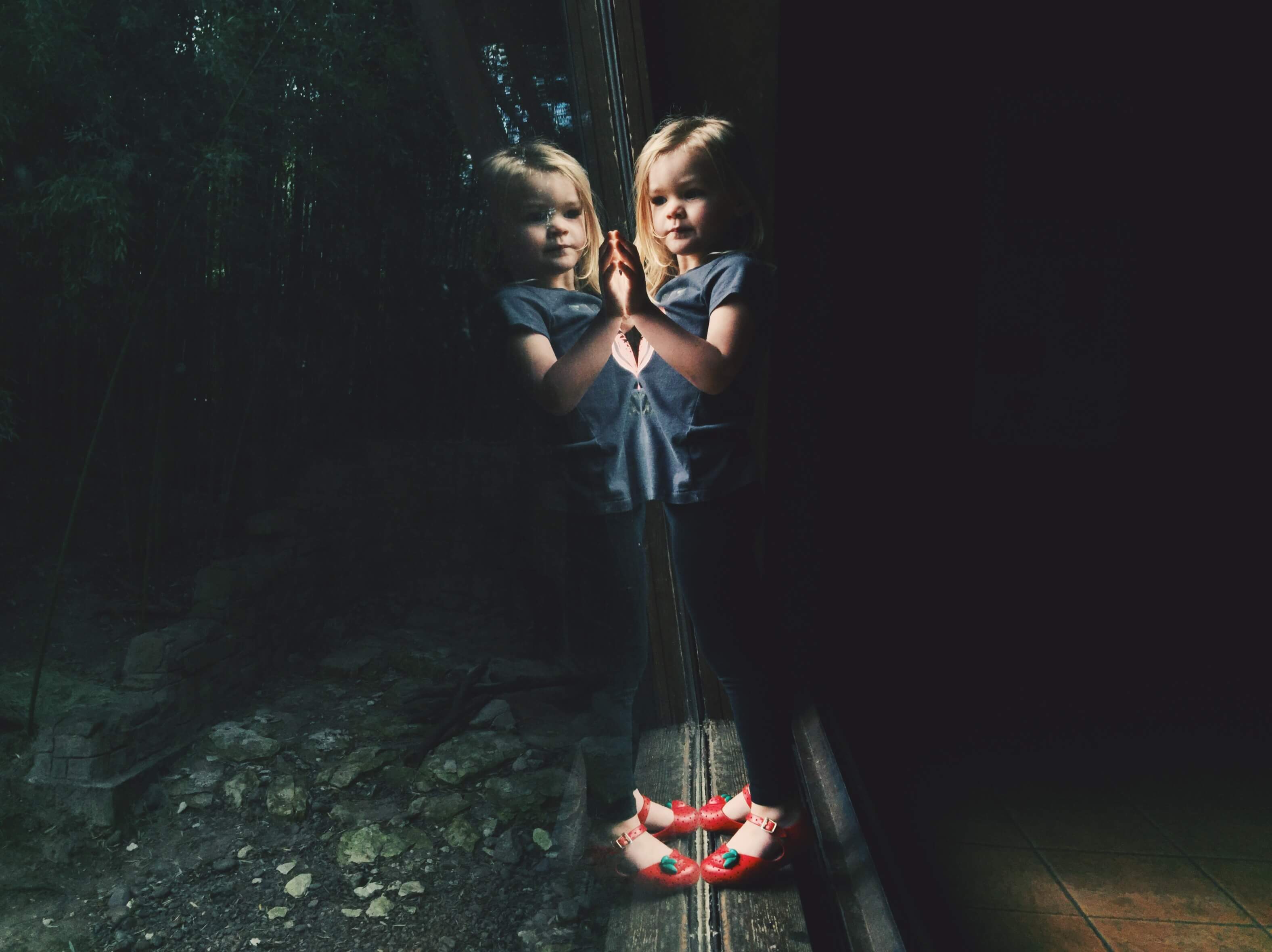 Little girl leaning against window and creating a reflection