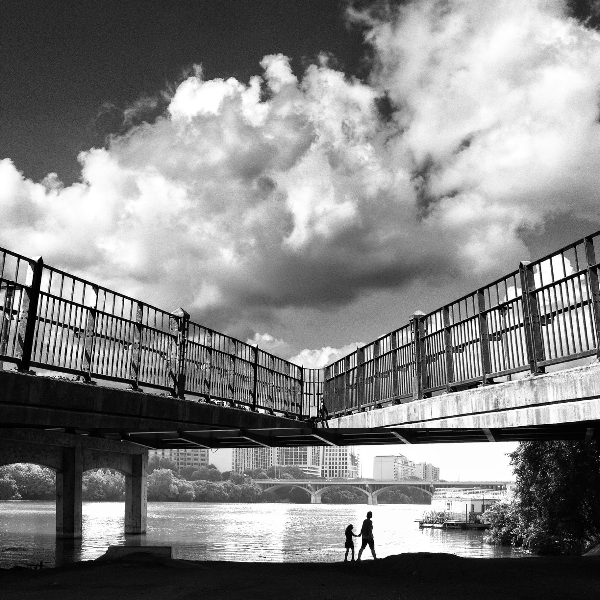 Inkedfingers photo in black and white of parent and child walking on waterfront below bridge