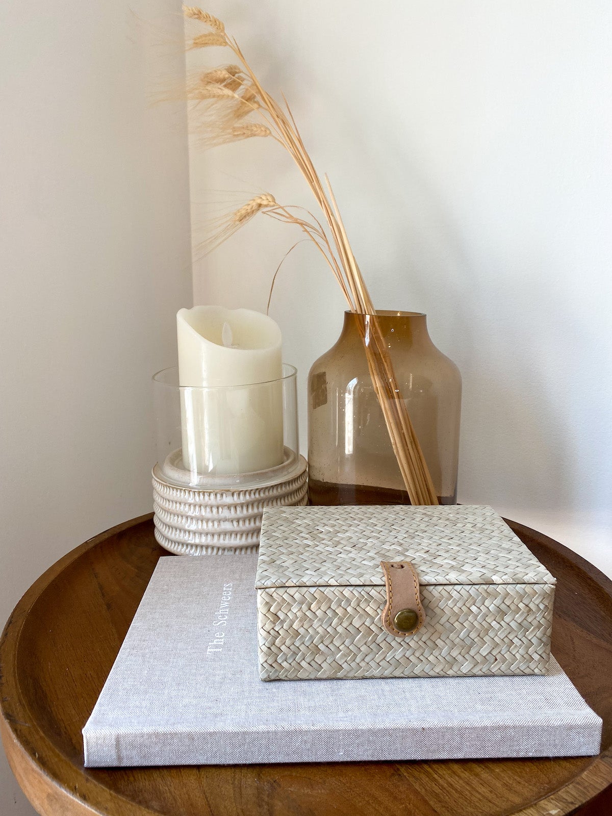 Circular side table with candle, dried straw in glass vase, and Artifact Uprising Layflat Photo Album