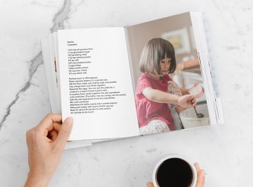 DIY recipe book opened to vanilla cupcake recipe with photo of little girl making cupcakes