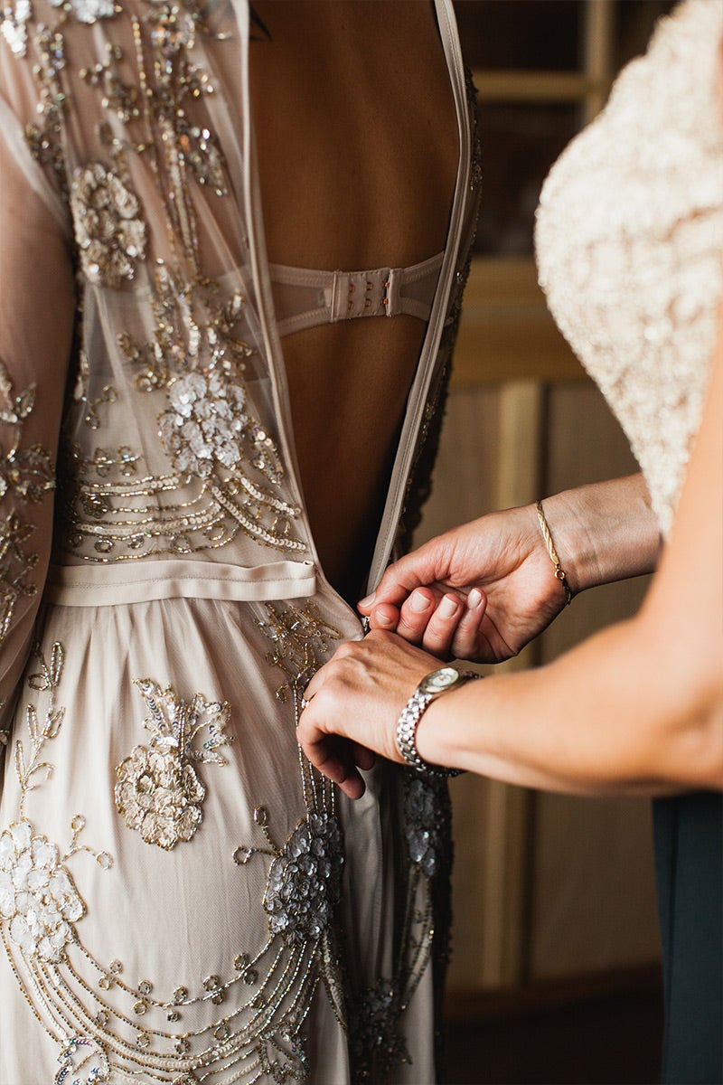 Mom zipping up bride's wedding gown