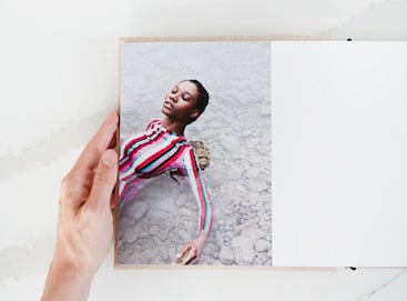 hand on edge of layflat photography portfolio book opened to image of woman in striped dress laying in shallow water