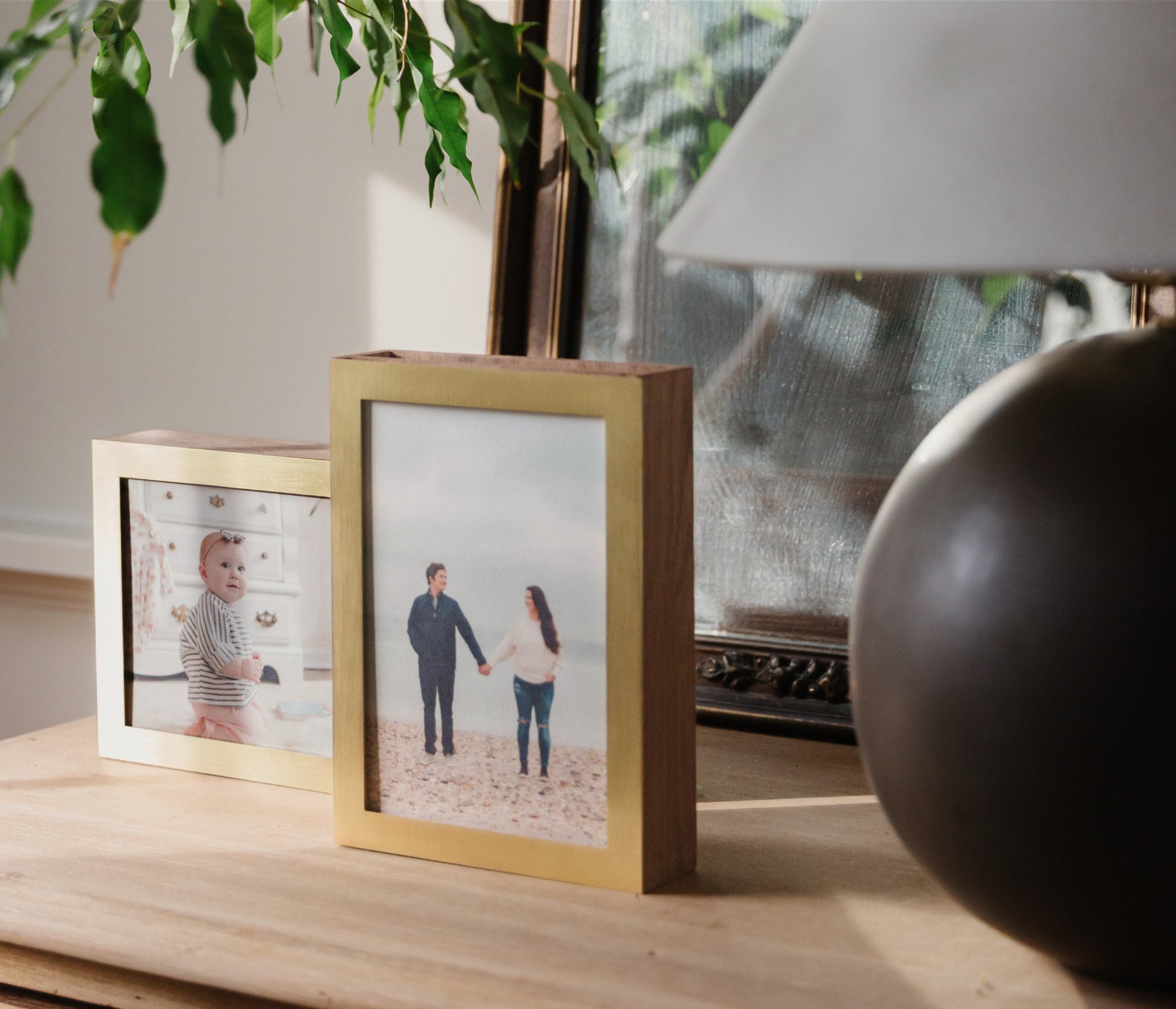 Two brass and wood display boxes showcasing two everyday prints with photo of a baby and a couple