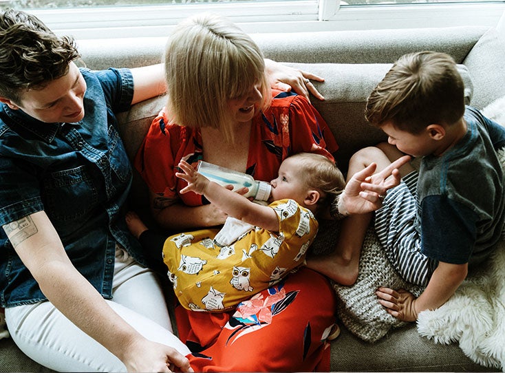 family with two moms and two kids snuggling in bed