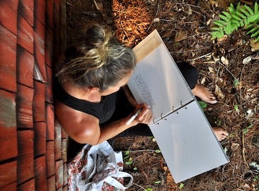 Liz young leaning against the rustic wall of a lakeside cottage and filling out prompts in the Artifact Uprising Early Years Book