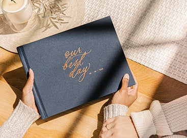 Hands holding Midnight Blue Wedding Layflat Album in sliver of light from window